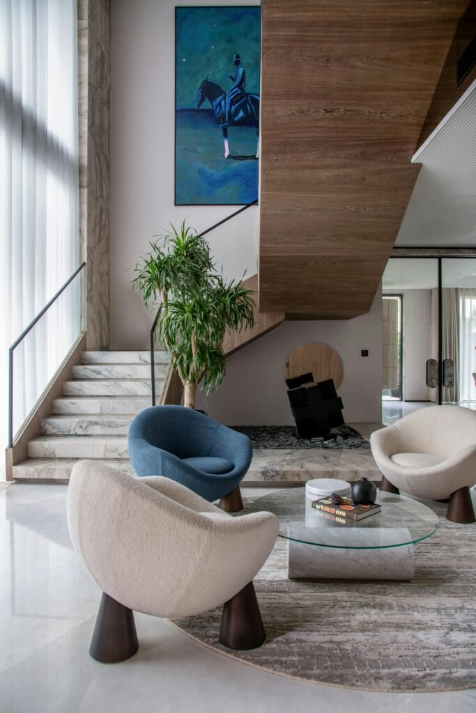 Elegant modern living room featuring unique chairs, art, and staircase for luxury appeal.